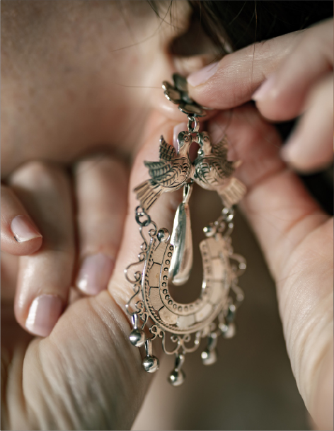 Close-up of hands fastening an ornate silver filigree bird earring