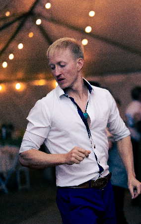 Man in a white shirt dances under string lights in a party tent