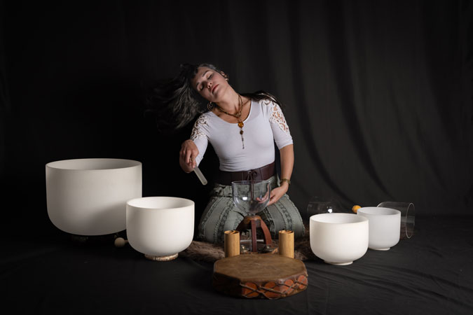 Sound healer tosses her hair while playing white crystal singing bowls