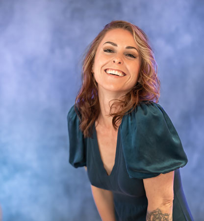 Laughing woman in a teal dress poses for a headshot on a blue backdrop