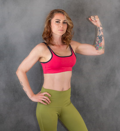 Fitness model in a pink sports bra flexes her tattooed arm