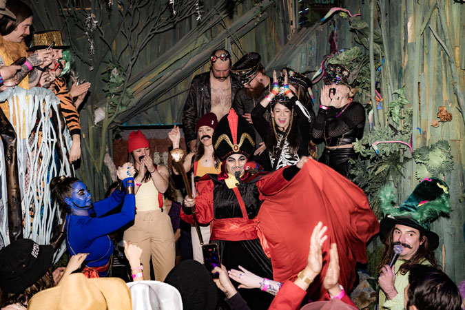 Costumed partygoers cheer around a man in a villain costume at a themed party