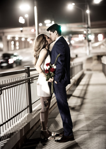 Couple kisses on a city overpass at night, holding red roses