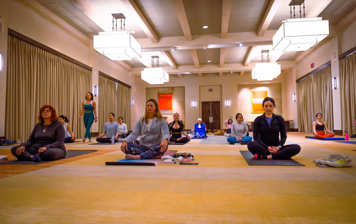 Group meditates on yoga mats in a large hotel ballroom