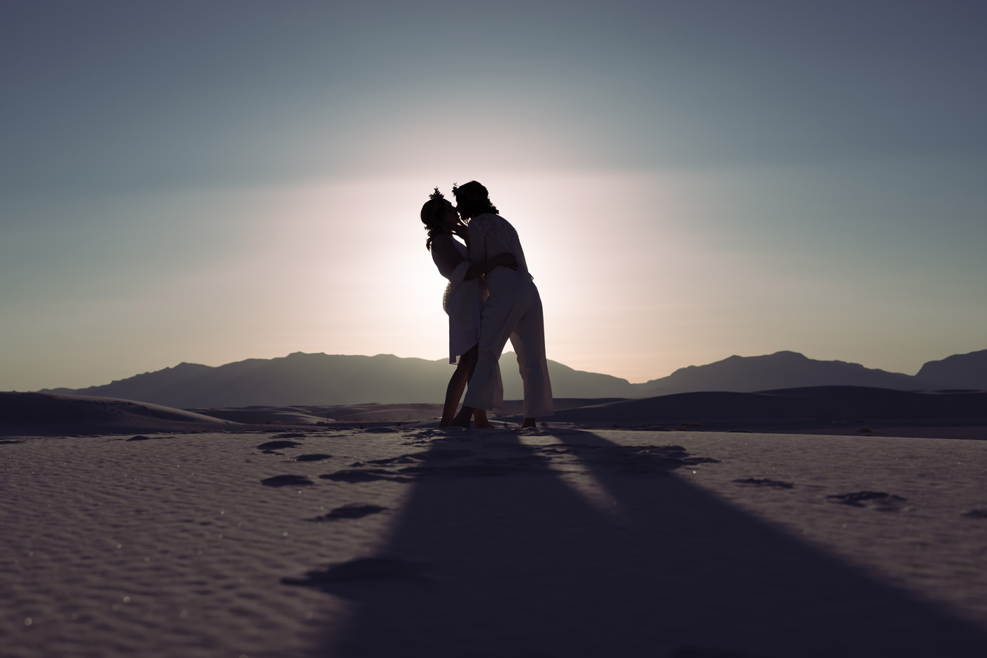 Couple silhouetted in a kiss on white sand dunes at sunset