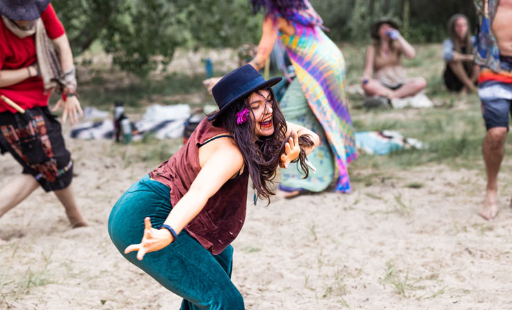Woman in a black hat dances barefoot on sand at an outdoor gathering