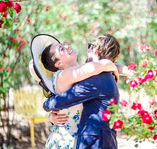 Couple in a joyful embrace among blooming red roses in a sunny garden