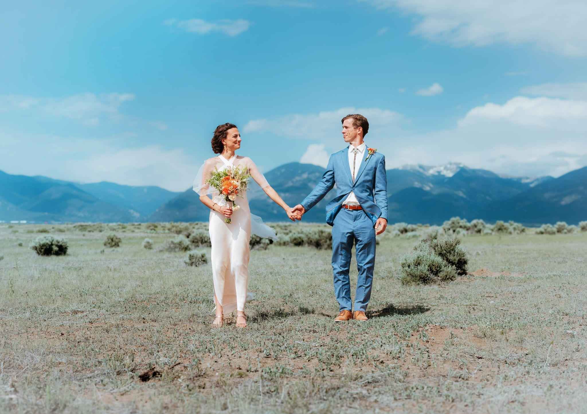Bride and groom hold hands in a sagebrush field below mountains