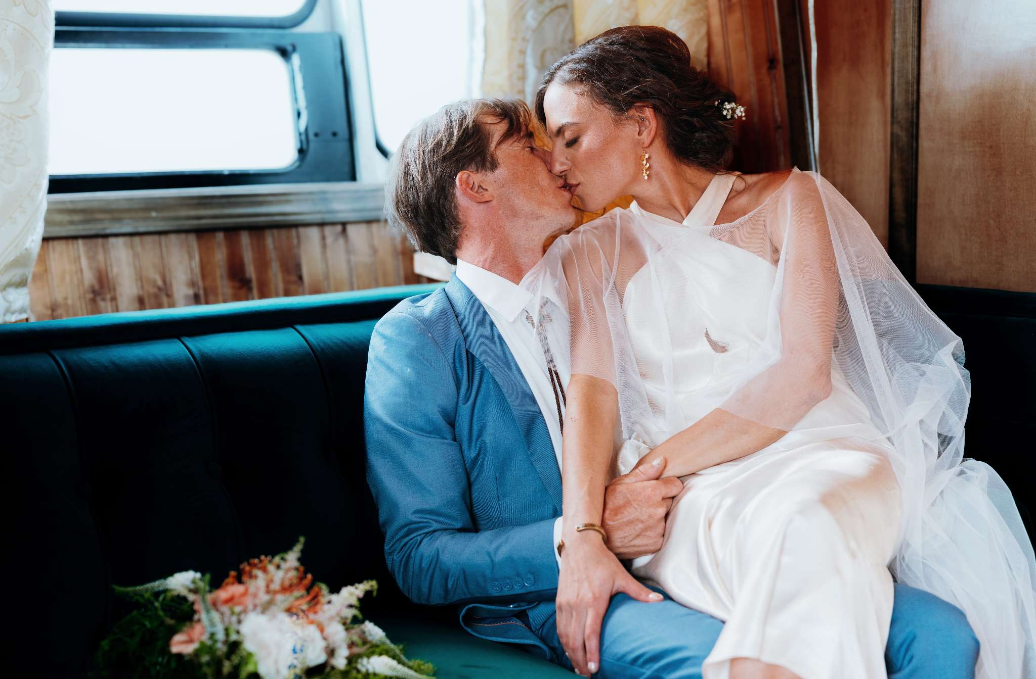 Bride and groom kiss on a teal bench inside a vintage trailer