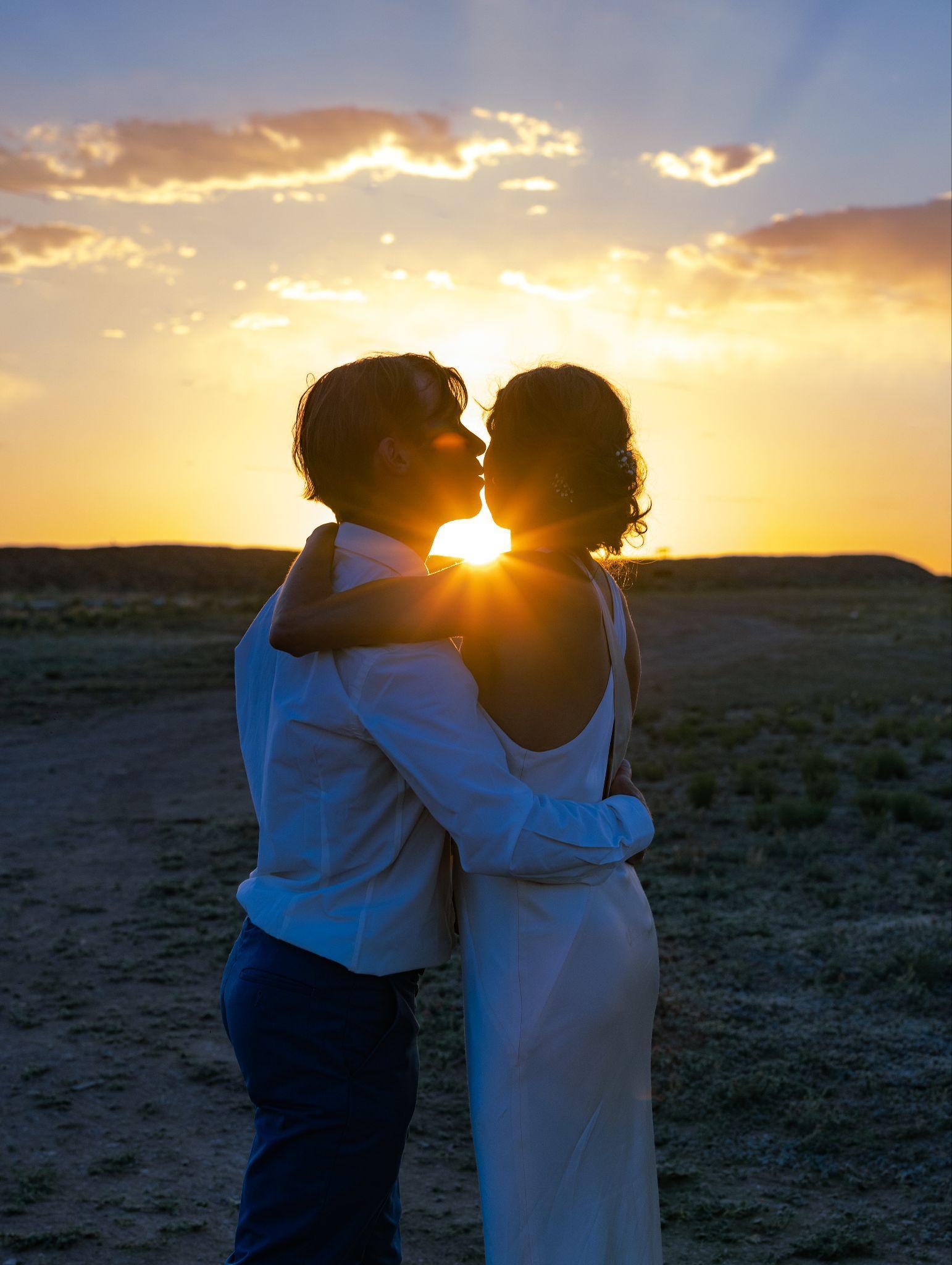 Bride and groom kiss as the sun sets behind them in the desert