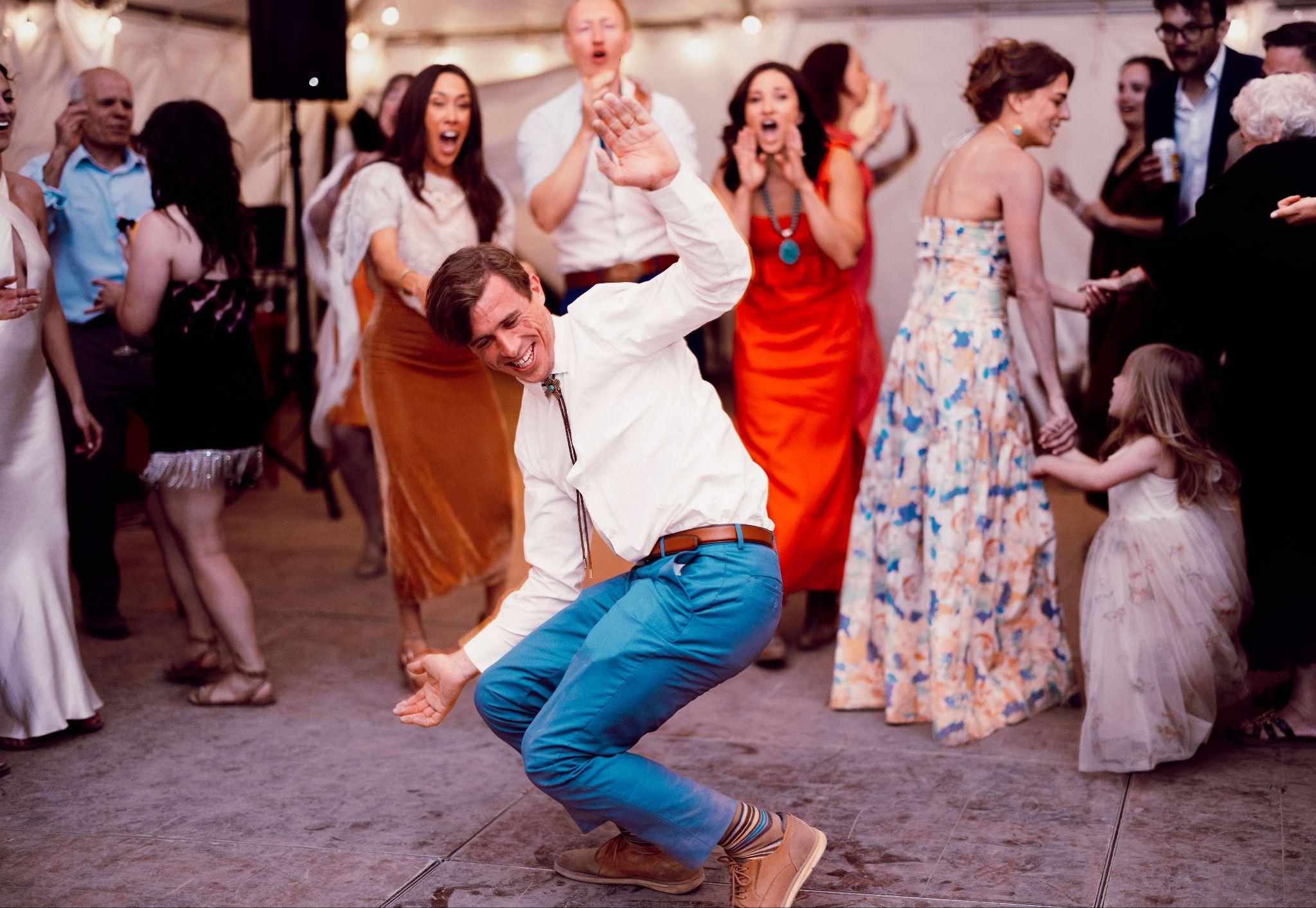 Groom in a bolo tie dances low as guests cheer in a reception tent