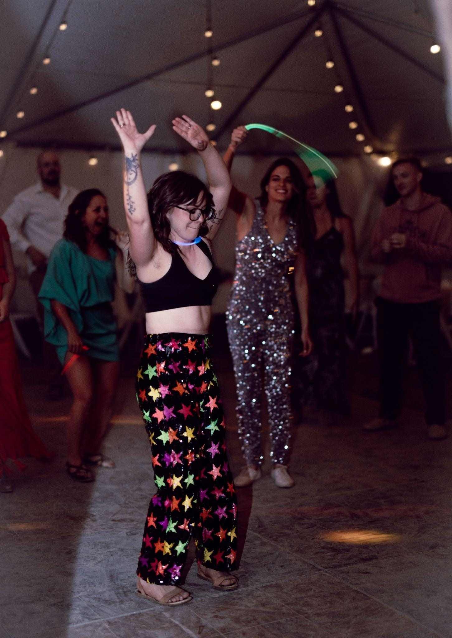 Guest in sparkly star pants dances with arms raised under tent lights