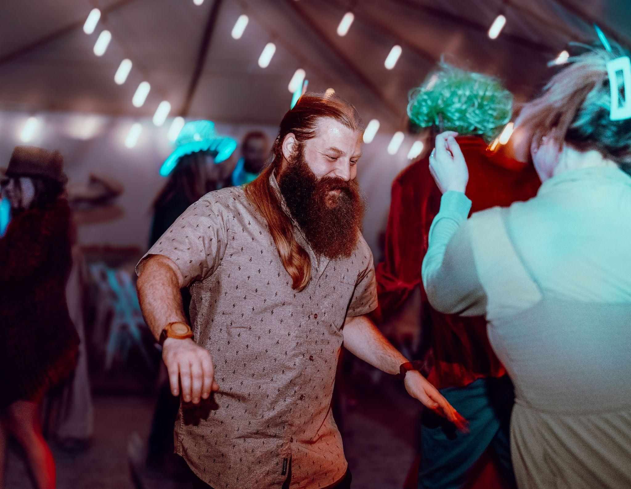 Bearded guest with long hair dances on a crowded reception dance floor