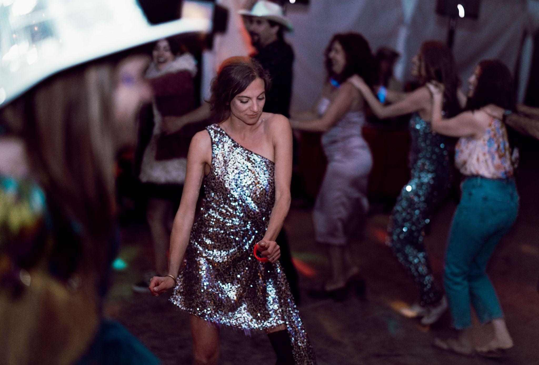 Woman in a sequin dress dances among guests at a night reception