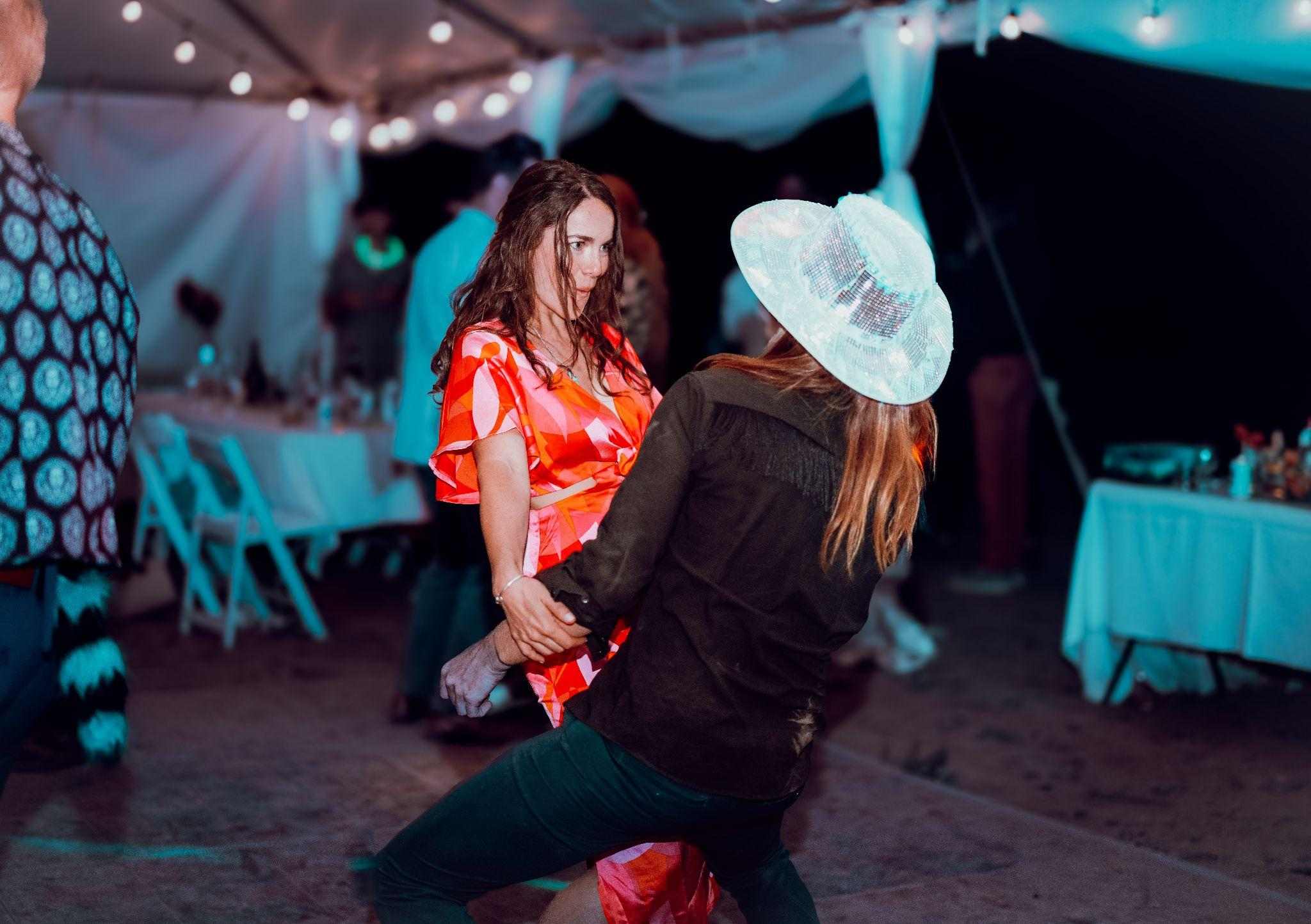 Two guests, one in a mirrored hat, dance together in a tent