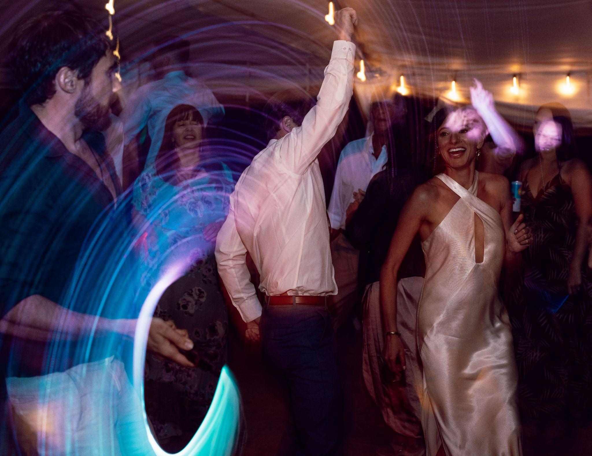 Bride in a satin halter dress dances with guests amid swirling lights