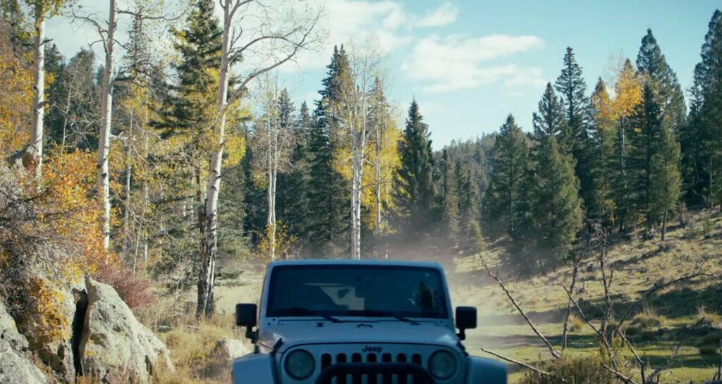 Jeep drives a dusty forest road through autumn aspens and pines