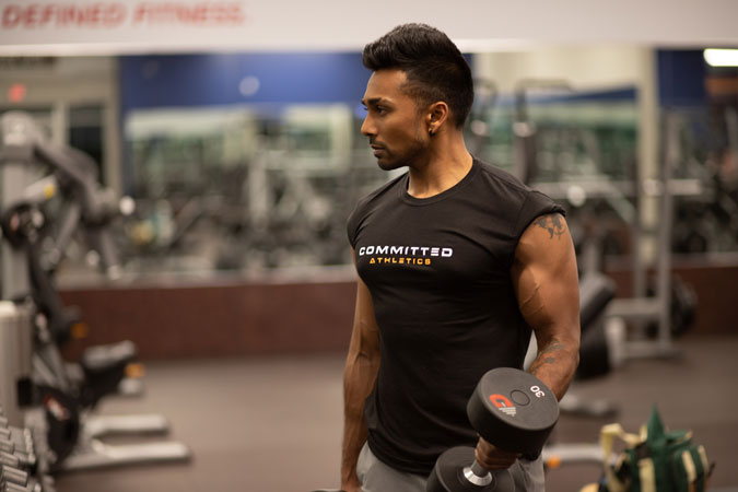 Man in a Committed Athletics shirt curls a dumbbell at Defined Fitness gym