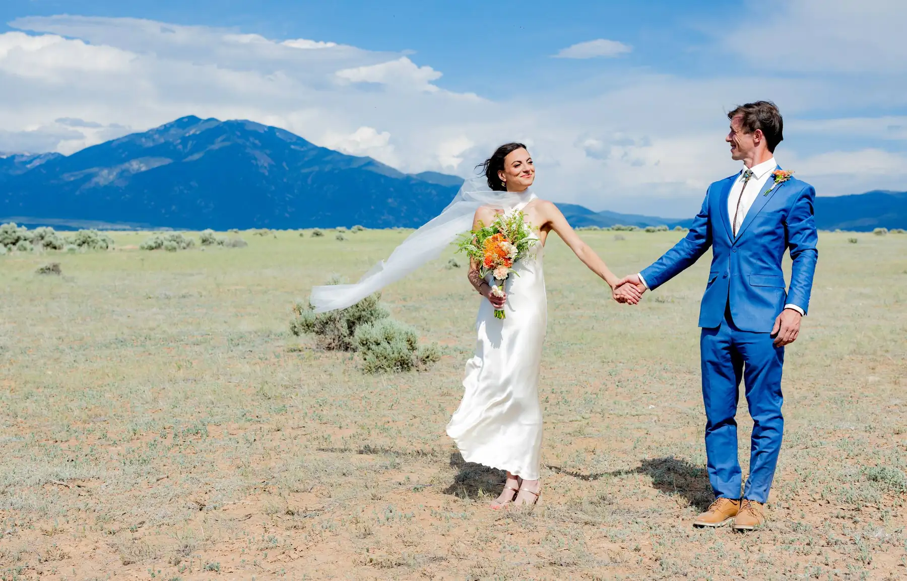 Bride and groom holding hands in a high desert field below the mountains