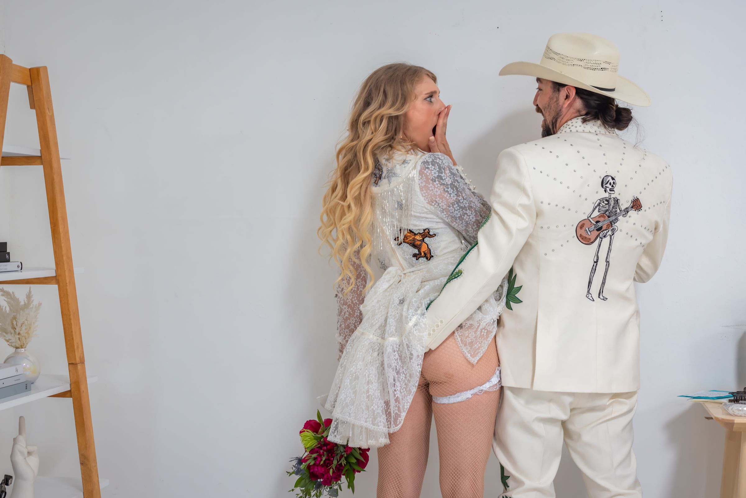 Bride gasping in surprise as the groom grabs a handful, against a white wall