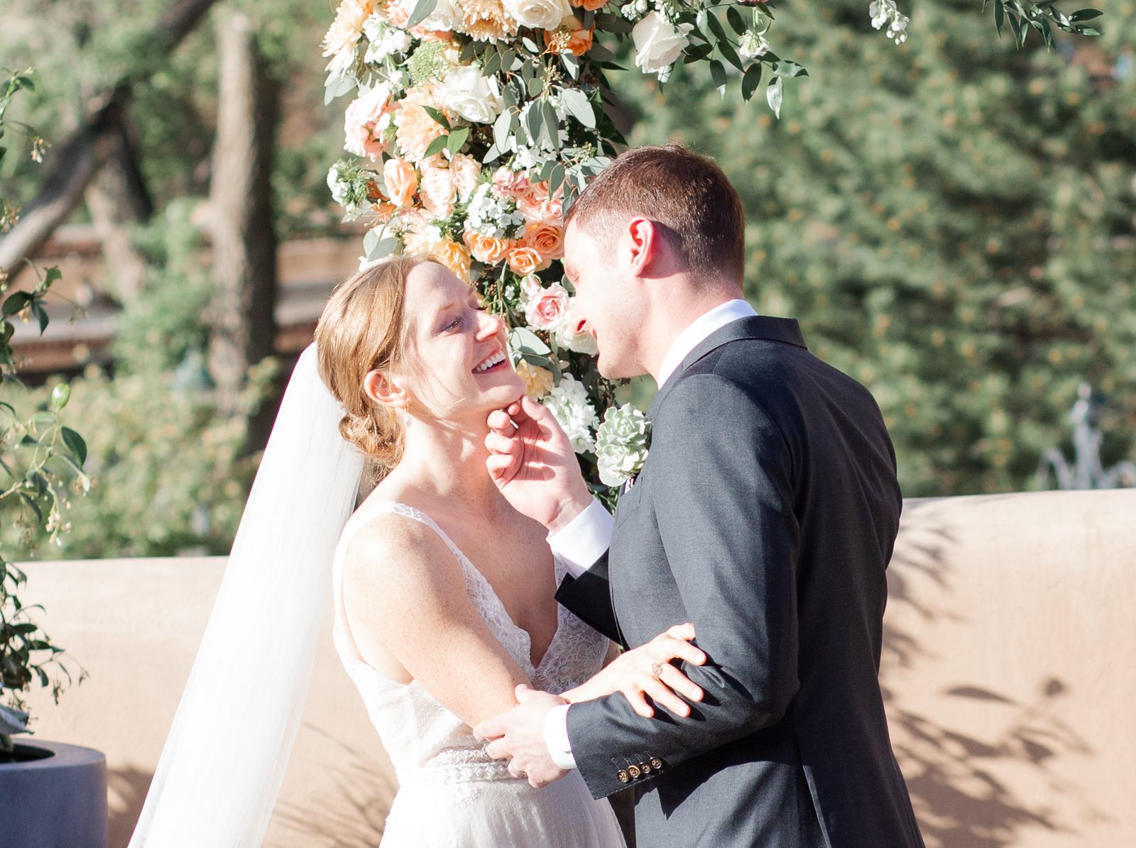 Bride laughing as the groom cradles her face beside a floral arch