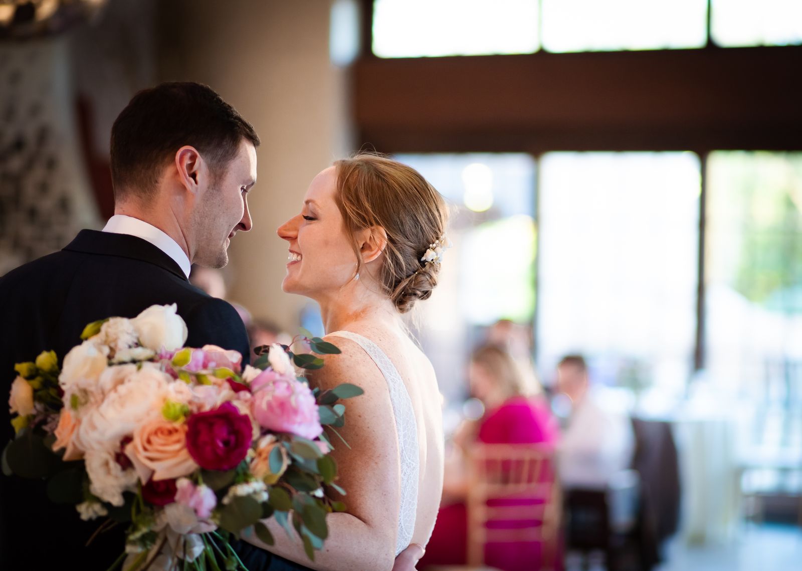 Bride holding a bouquet smiling at the groom in a reception hall