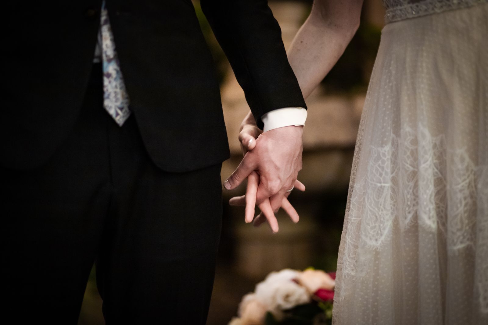 Close up of the couple holding hands, dark suit against a lace dress