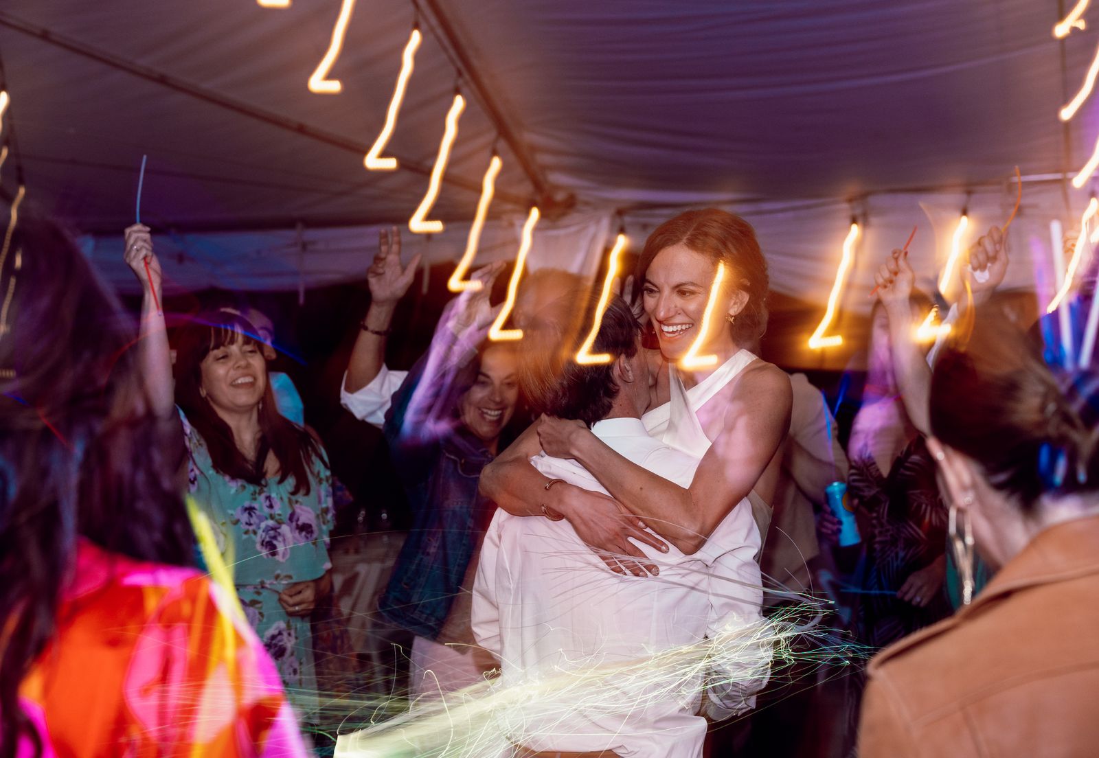 Bride dancing with friends under string lights at the reception
