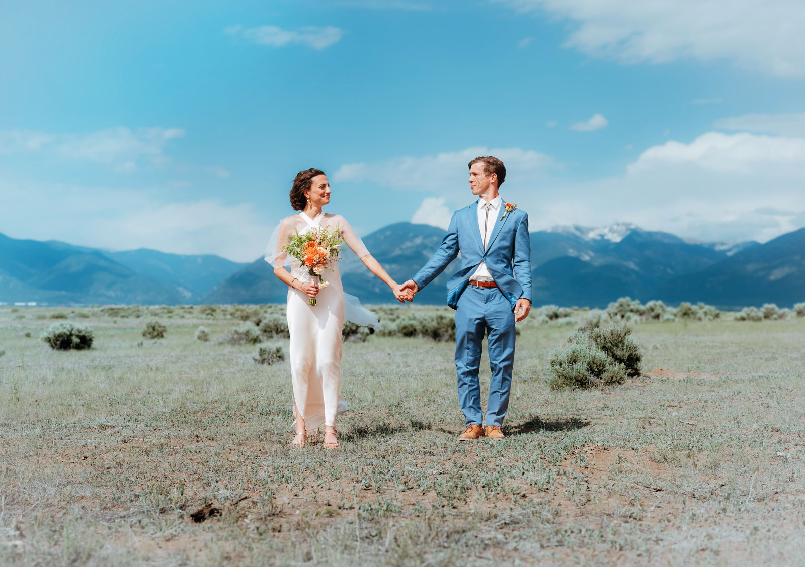 Bride and groom holding hands in a sagebrush field before blue mountains