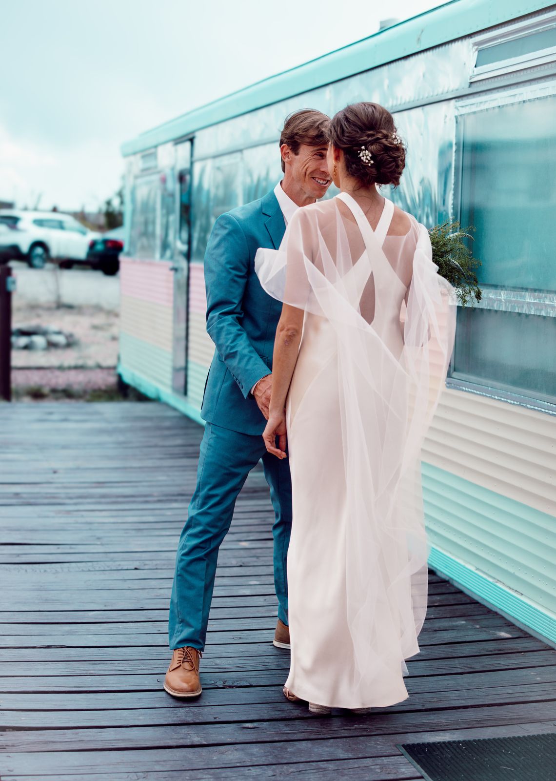Couple sharing a close moment on a boardwalk beside a vintage trailer