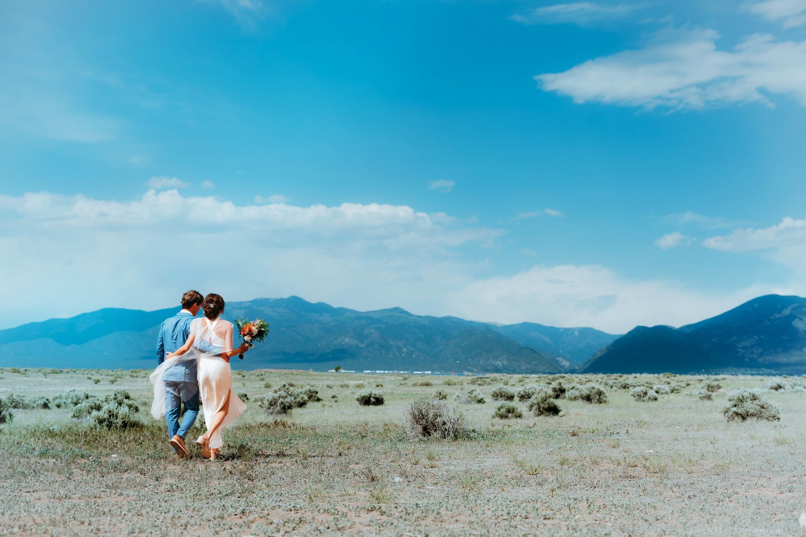Couple walking arm in arm toward distant mountains under a wide blue sky