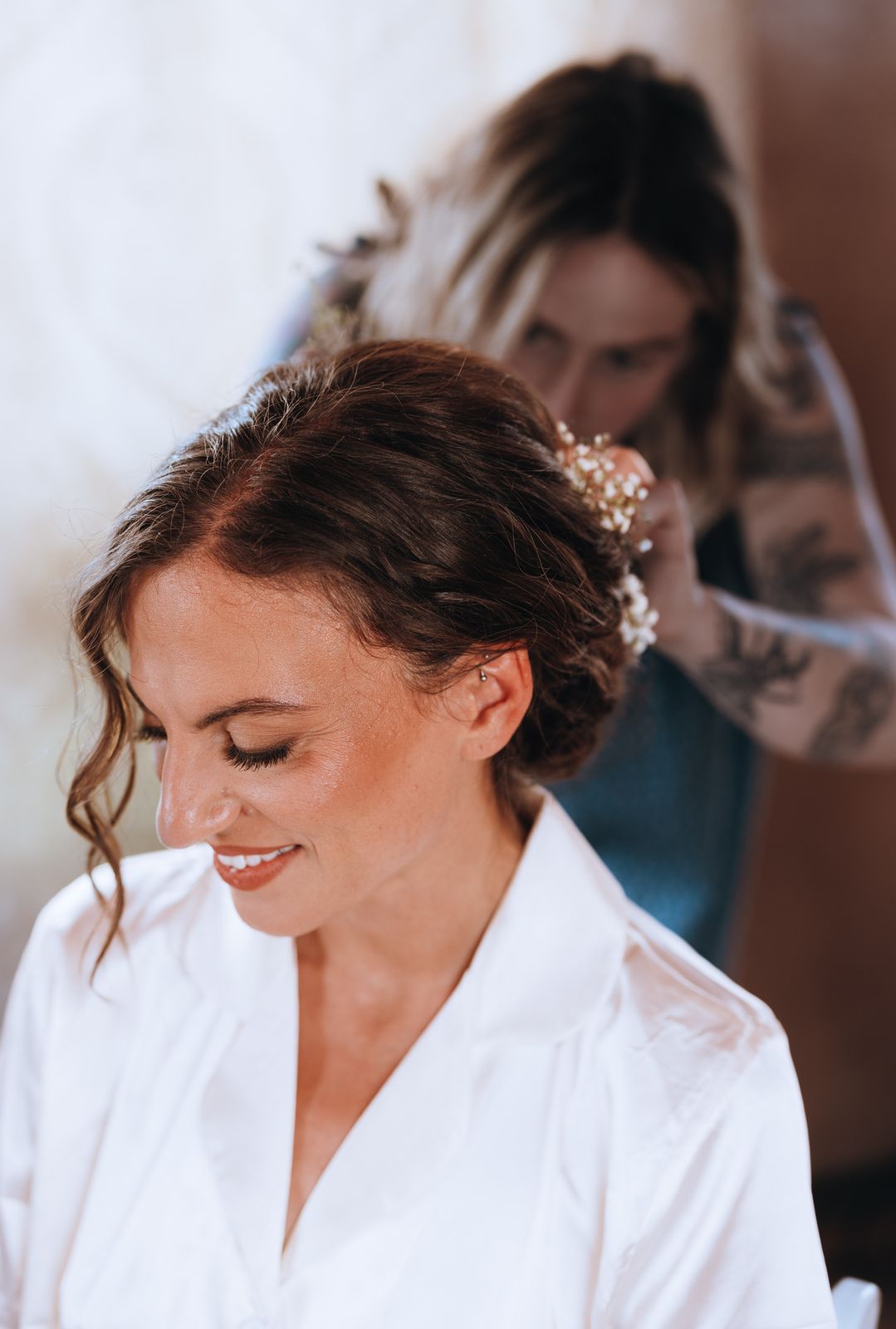 Bride smiling down while a friend pins flowers into her hair