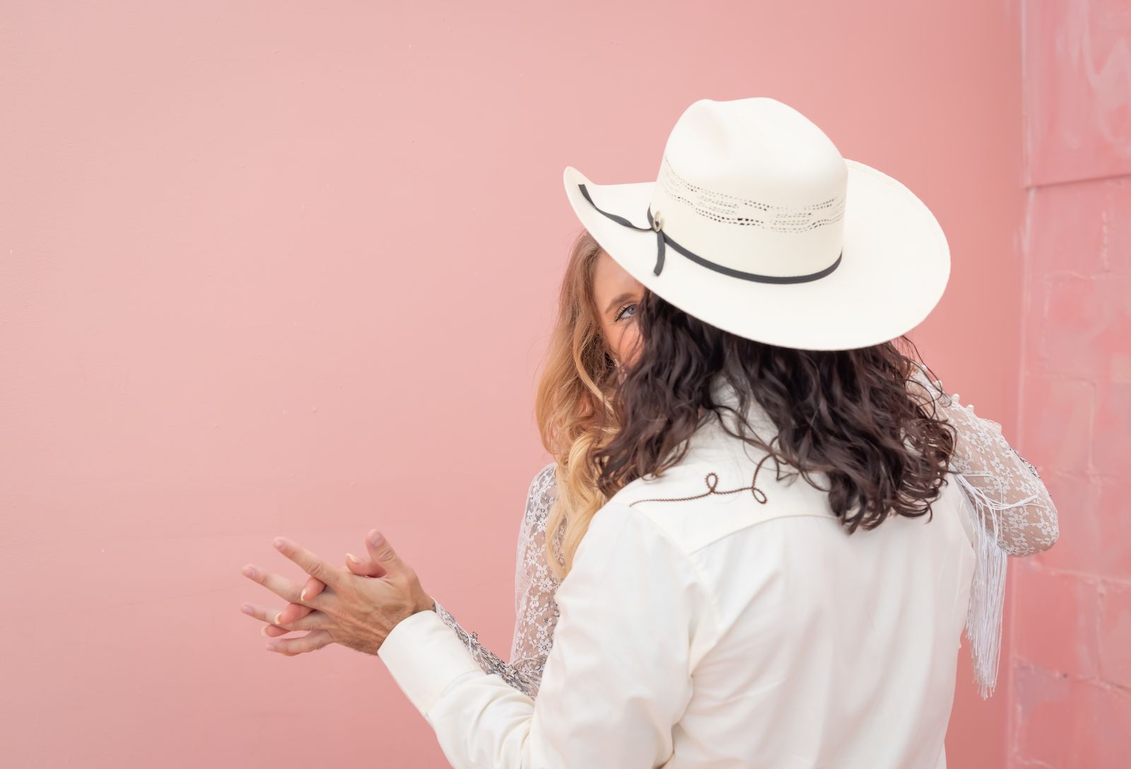 Groom in a white cowboy hat clapping, seen from behind against a pink wall
