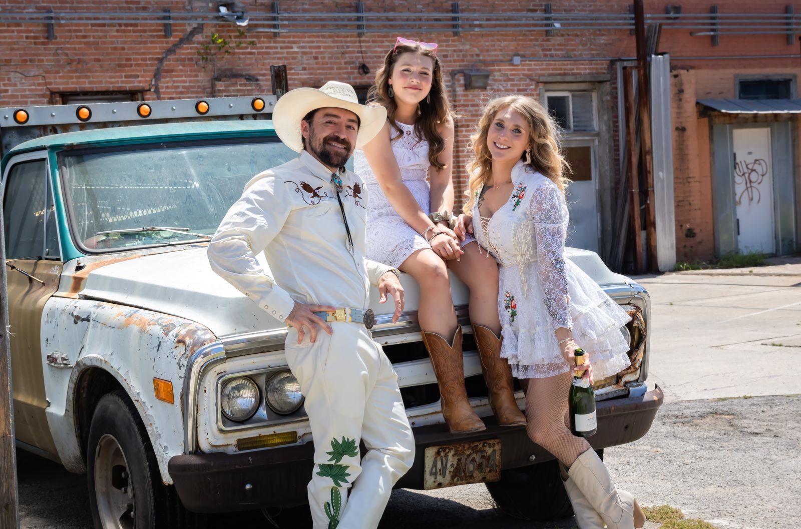 Couple and a young girl sitting on the hood of a vintage pickup truck