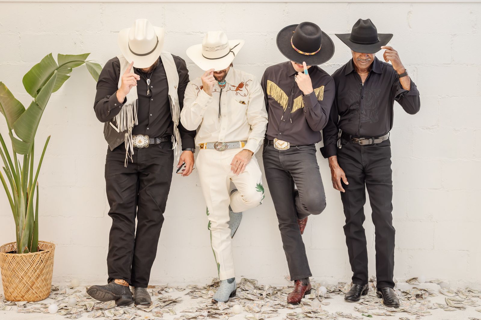 Four groomsmen in cowboy hats tipping their brims against a white wall