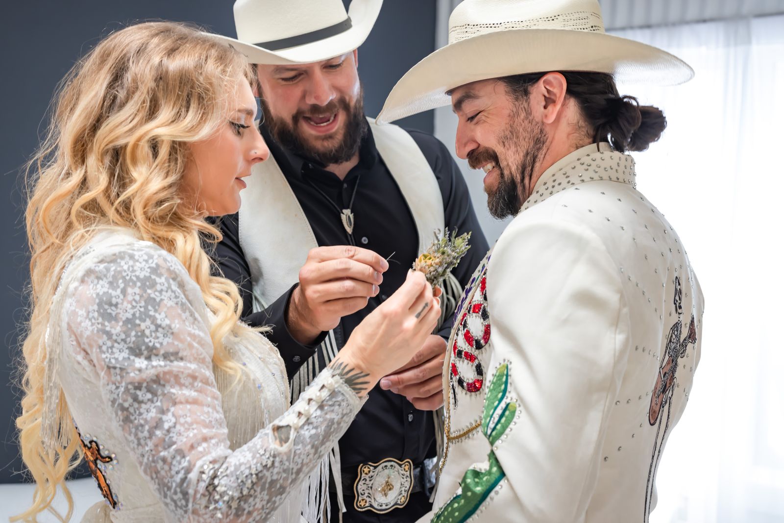 Bride and groom laughing as a friend pins on a boutonniere
