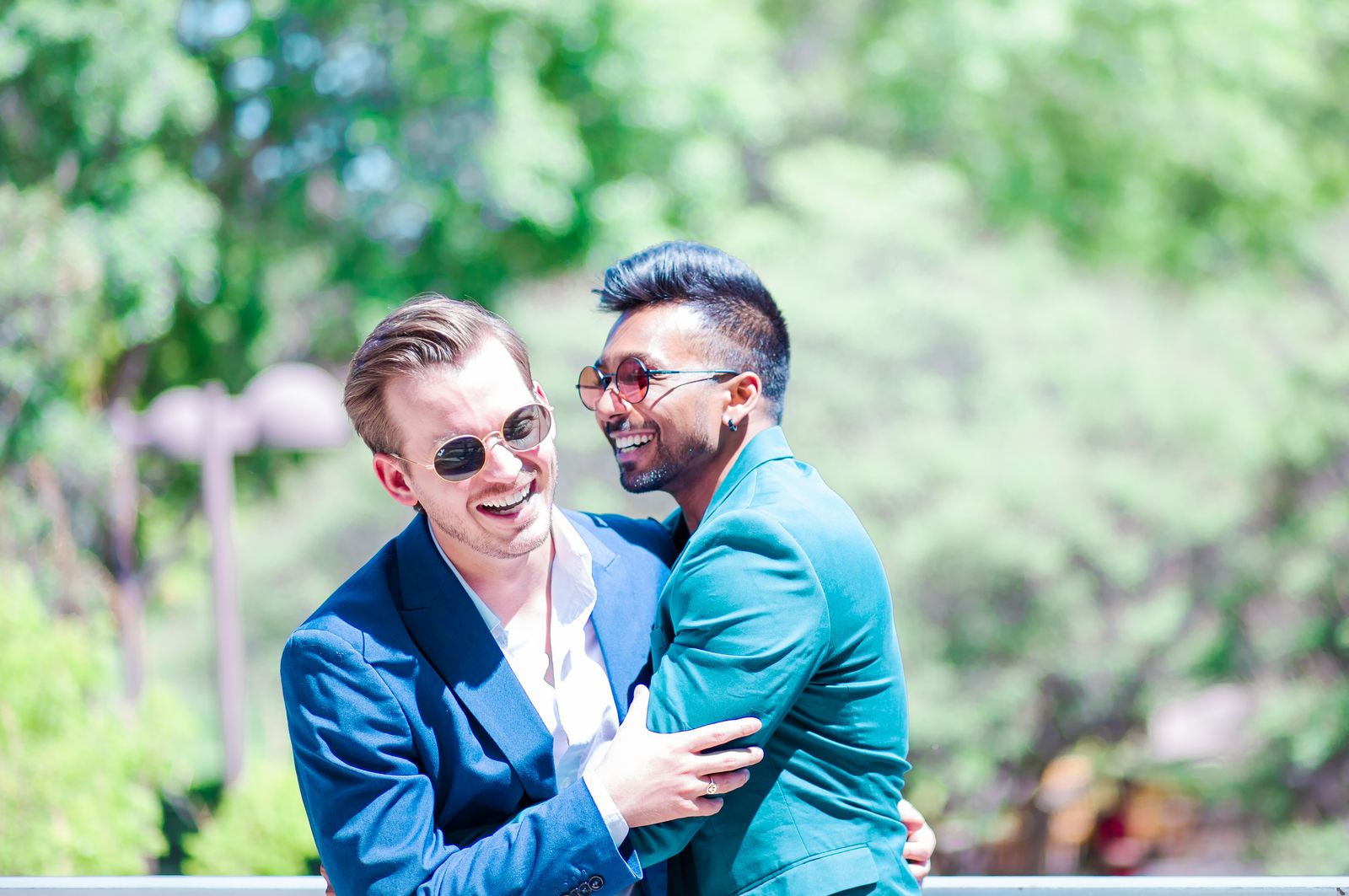 Two grooms laughing and hugging in a sunny garden