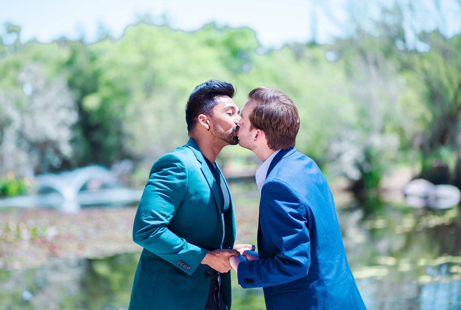 Two grooms kissing beside a garden pond