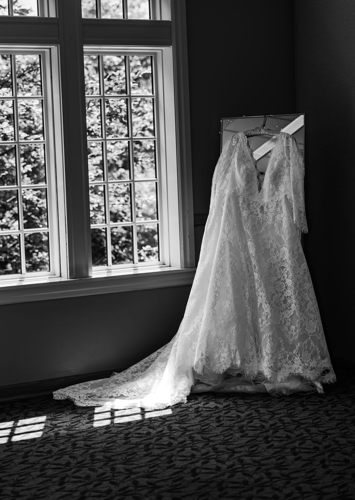 Black and white photo of a lace wedding dress hanging by a window