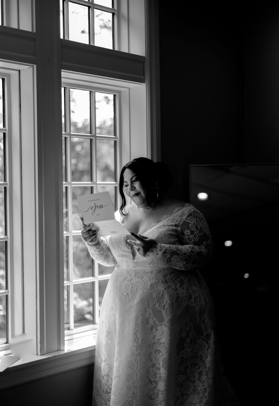 Black and white photo of the bride reading a letter by a window