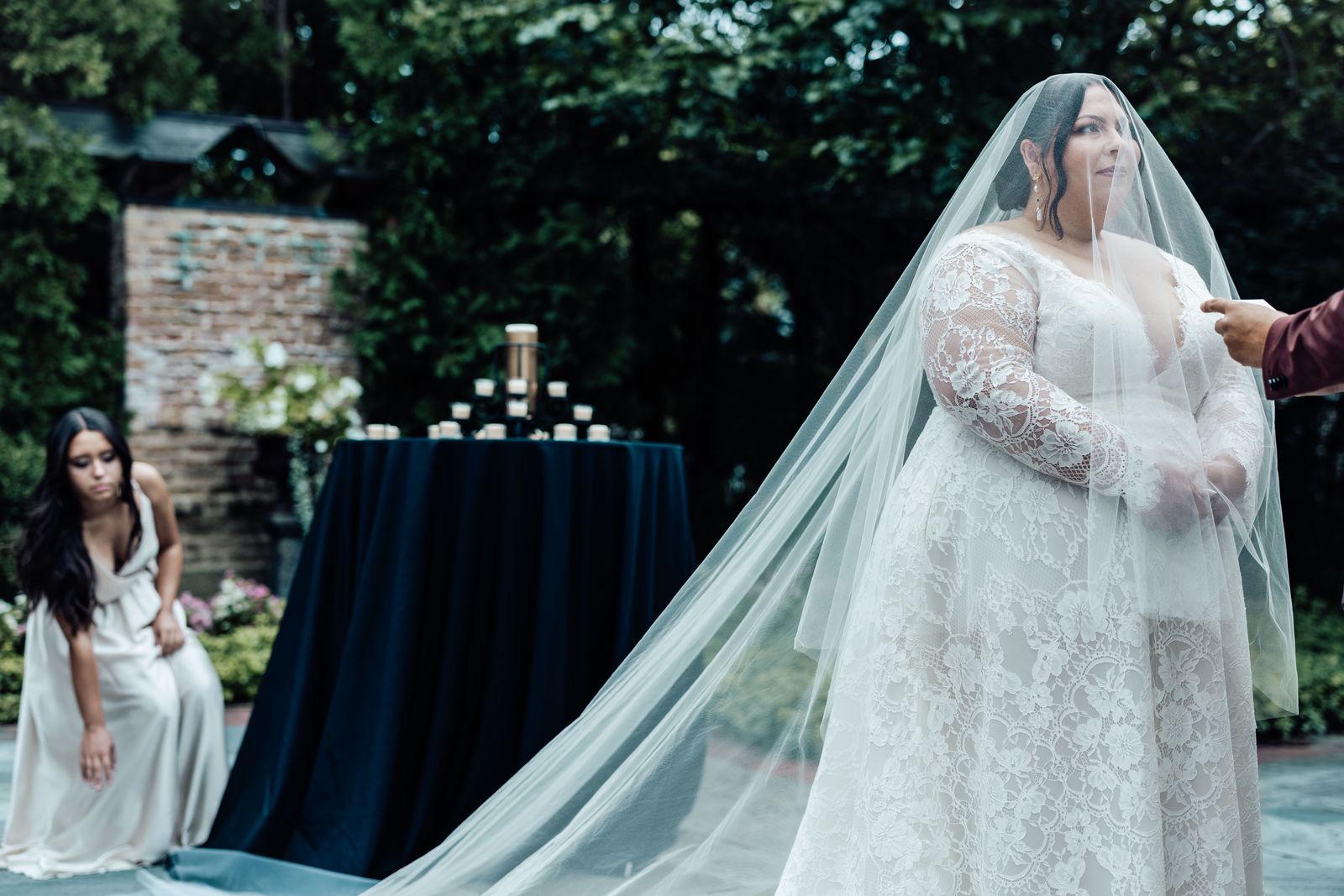 Bride in a long veil at an outdoor ceremony with a bridesmaid seated behind