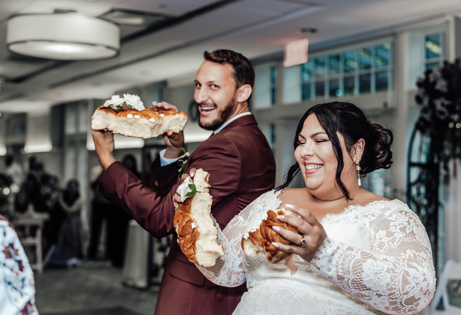 Bride and groom laughing as they hold up a large decorated bread loaf