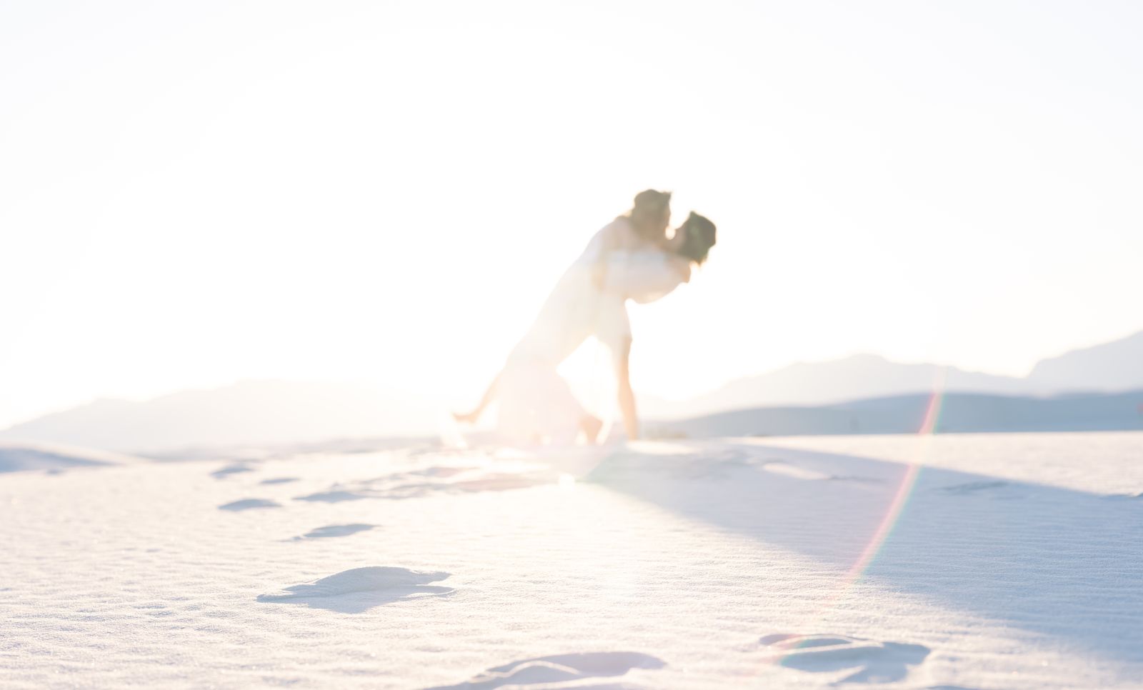 Sunlit silhouette of the couple kissing on bright white sand