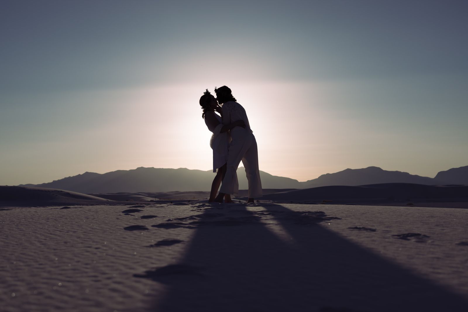 Silhouette of the couple embracing at sunset with long shadows on the dunes