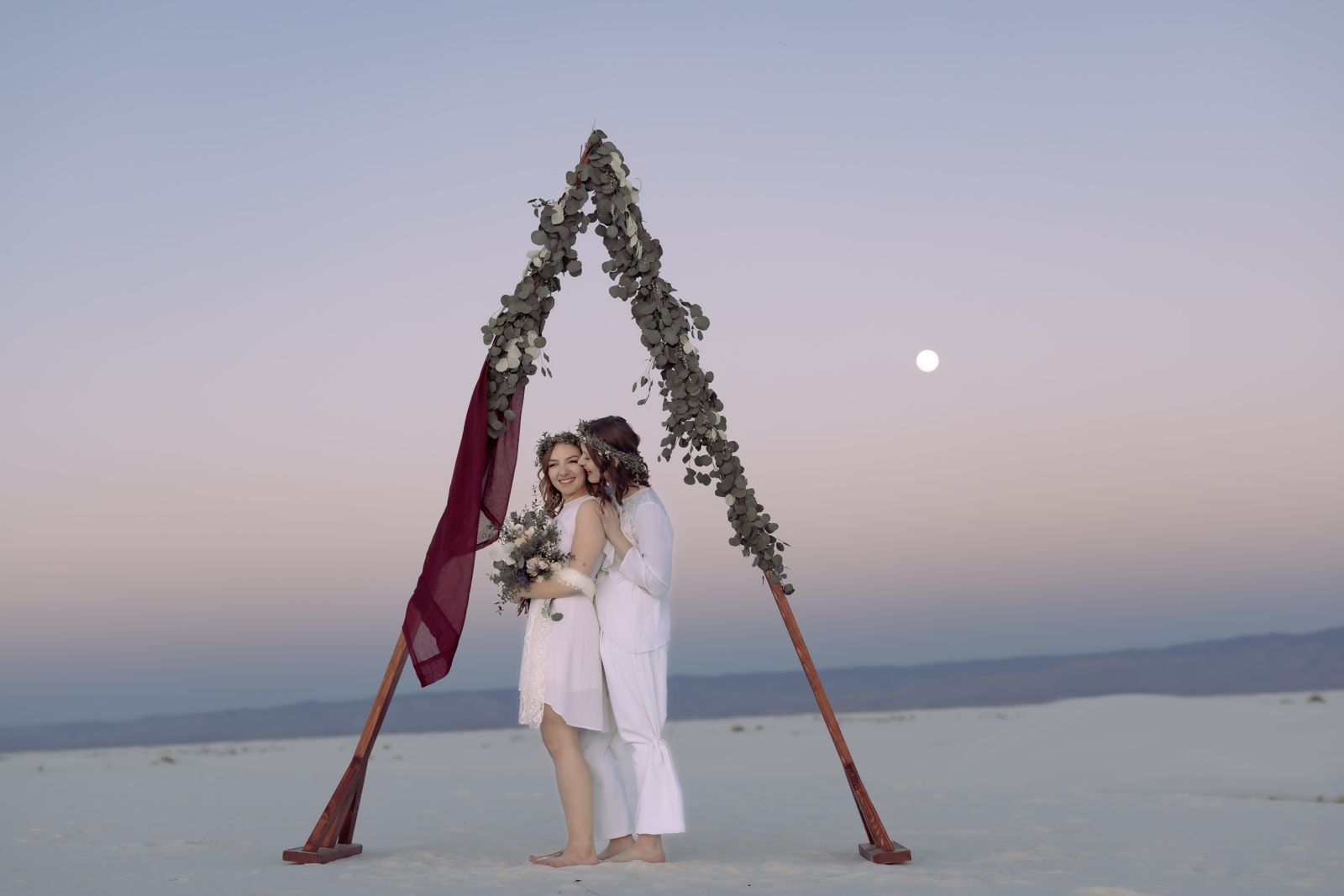 Floral arch with a draped red cloth on the white sand dunes