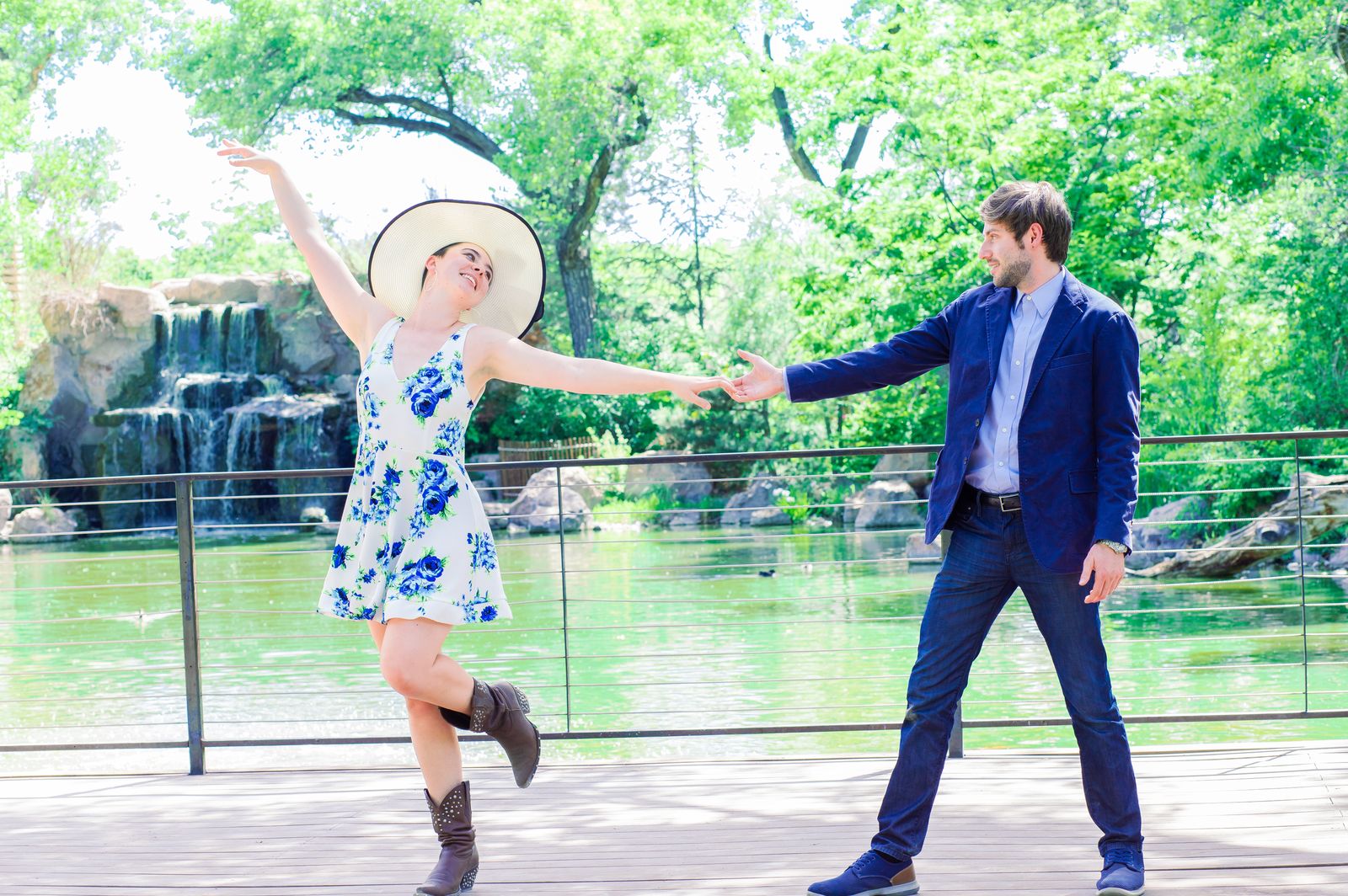 Couple holding hands playfully beside a pond and waterfall